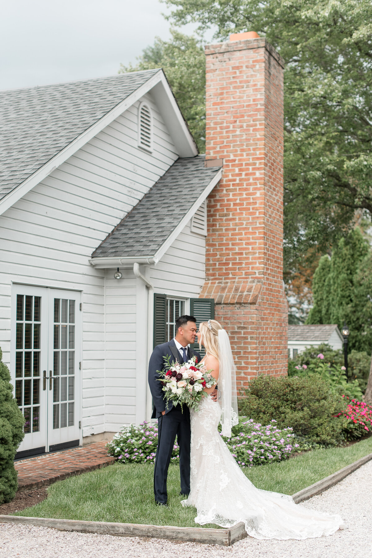 Bride and Groom smiling at each other in front of white house with brick chimney