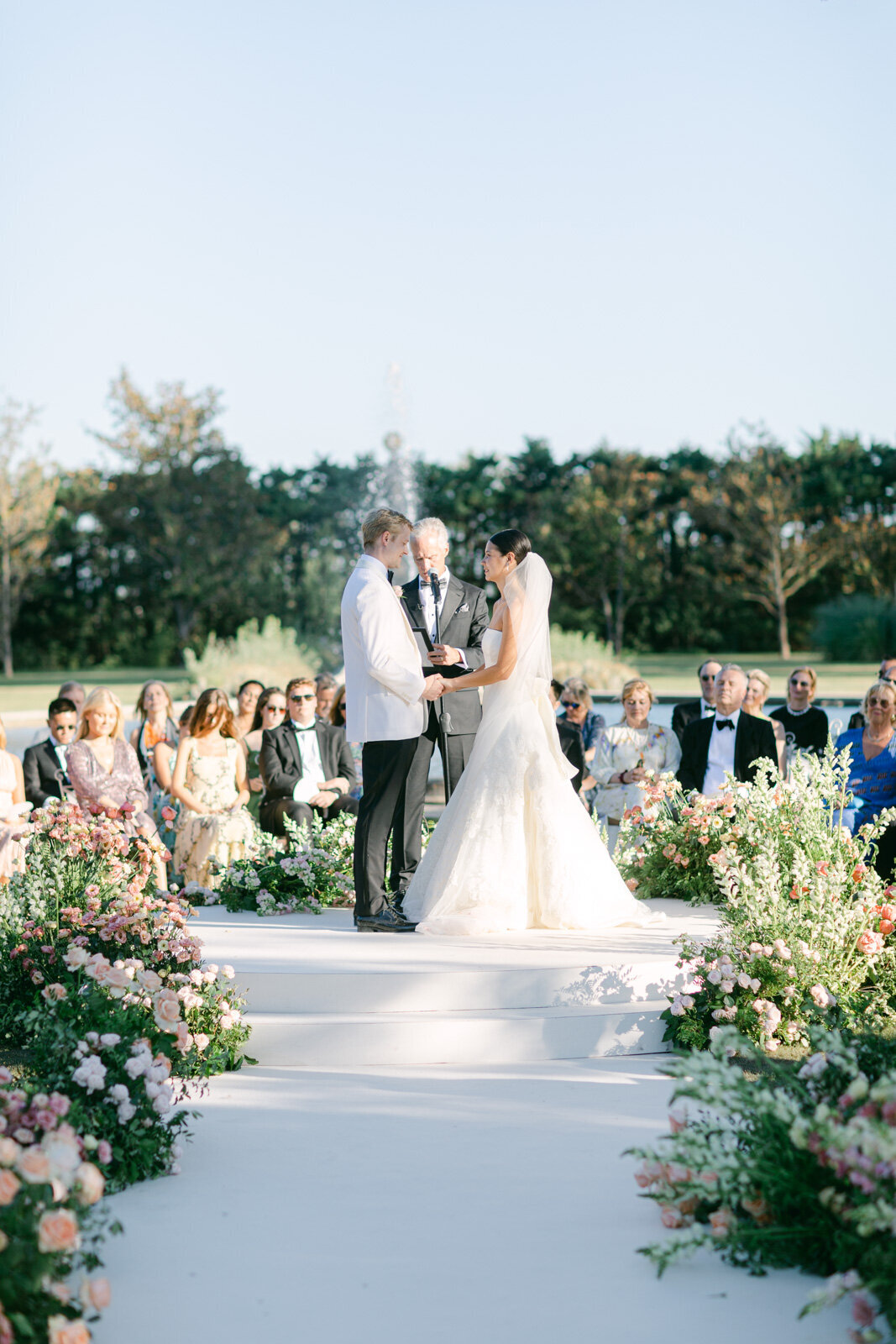 Bride and groom exchanging vows at outdoor wedding ceremony in Provence surrounded by floral arrangements.