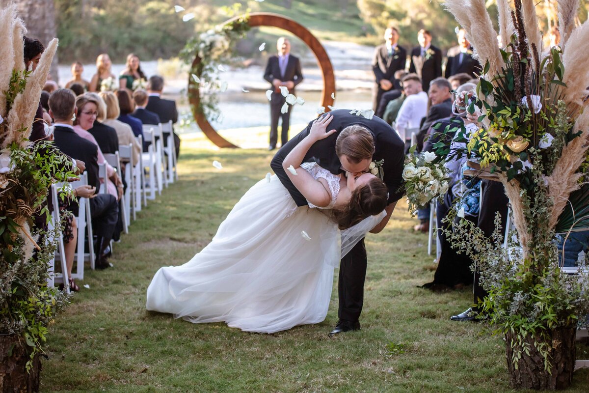 groom dips bride while petals fly at end of the aisle after ceremony