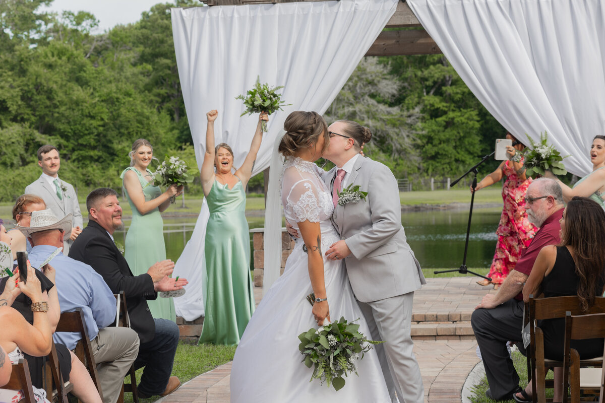 brides kissing in the aisle with family celebrating in the background at Cypress Creek Farmhouse by Orlando Florida Wedding Photographer Amanda Richardson Photography