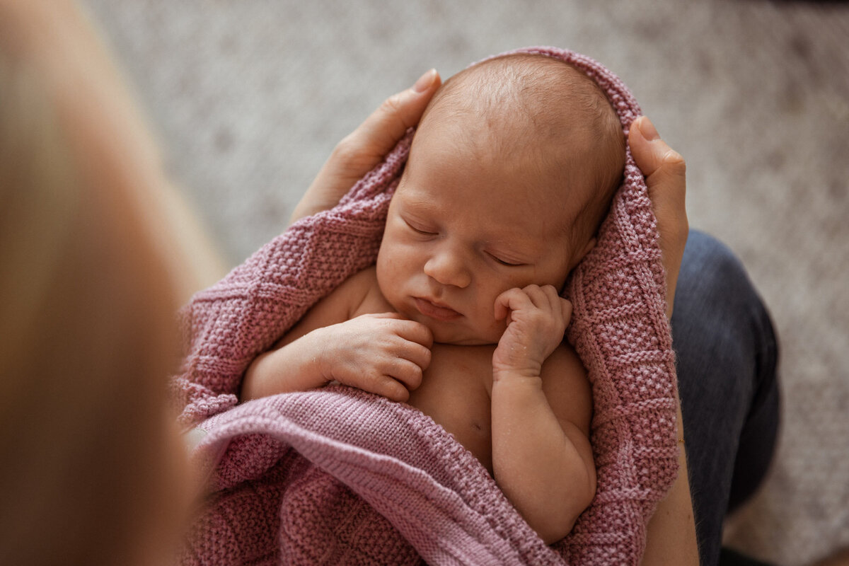 Livsstilsfoto nærbilde av en baby som ligger på mors knær inntullet i et rosa strikket pledd.