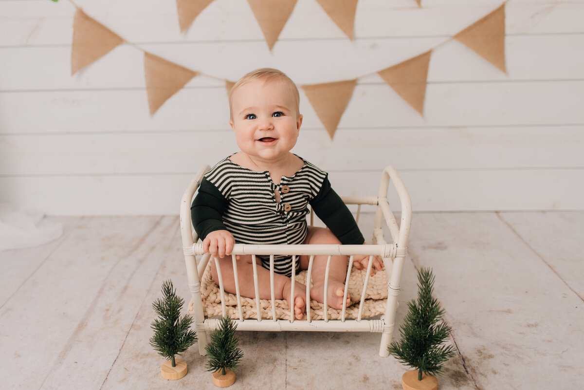 Six month old boy in green smiling at camera with rustic set