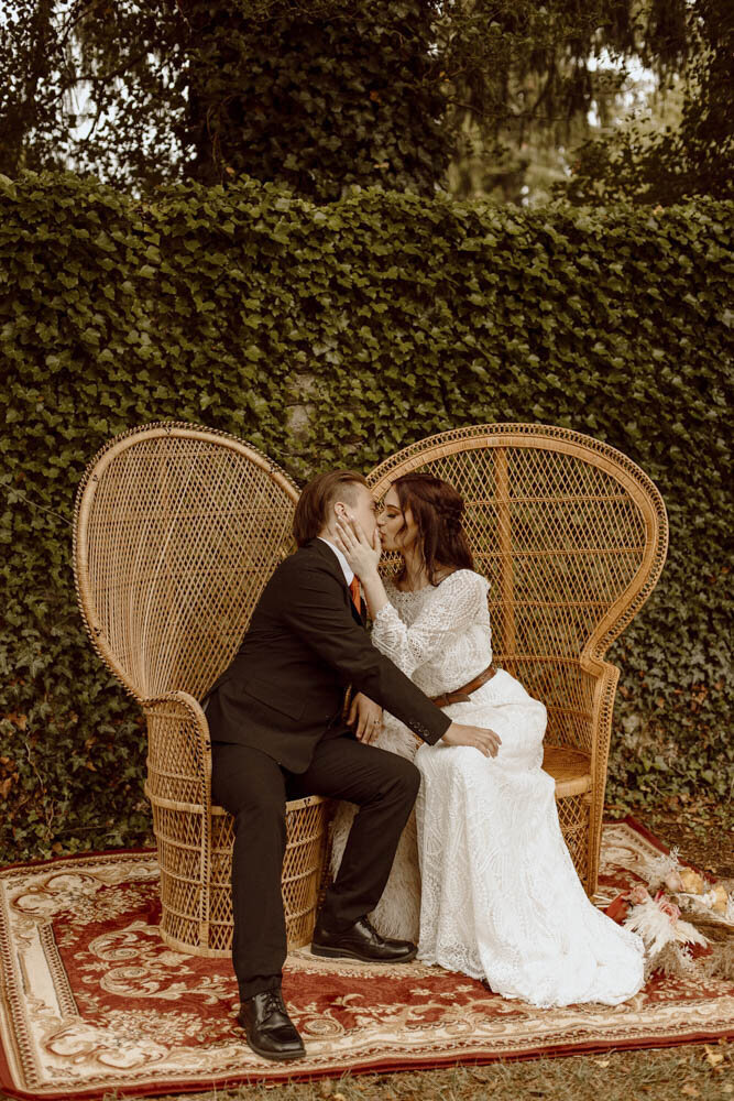 Boho Wedding couple sits in boho rattan wicker peacock chairs.