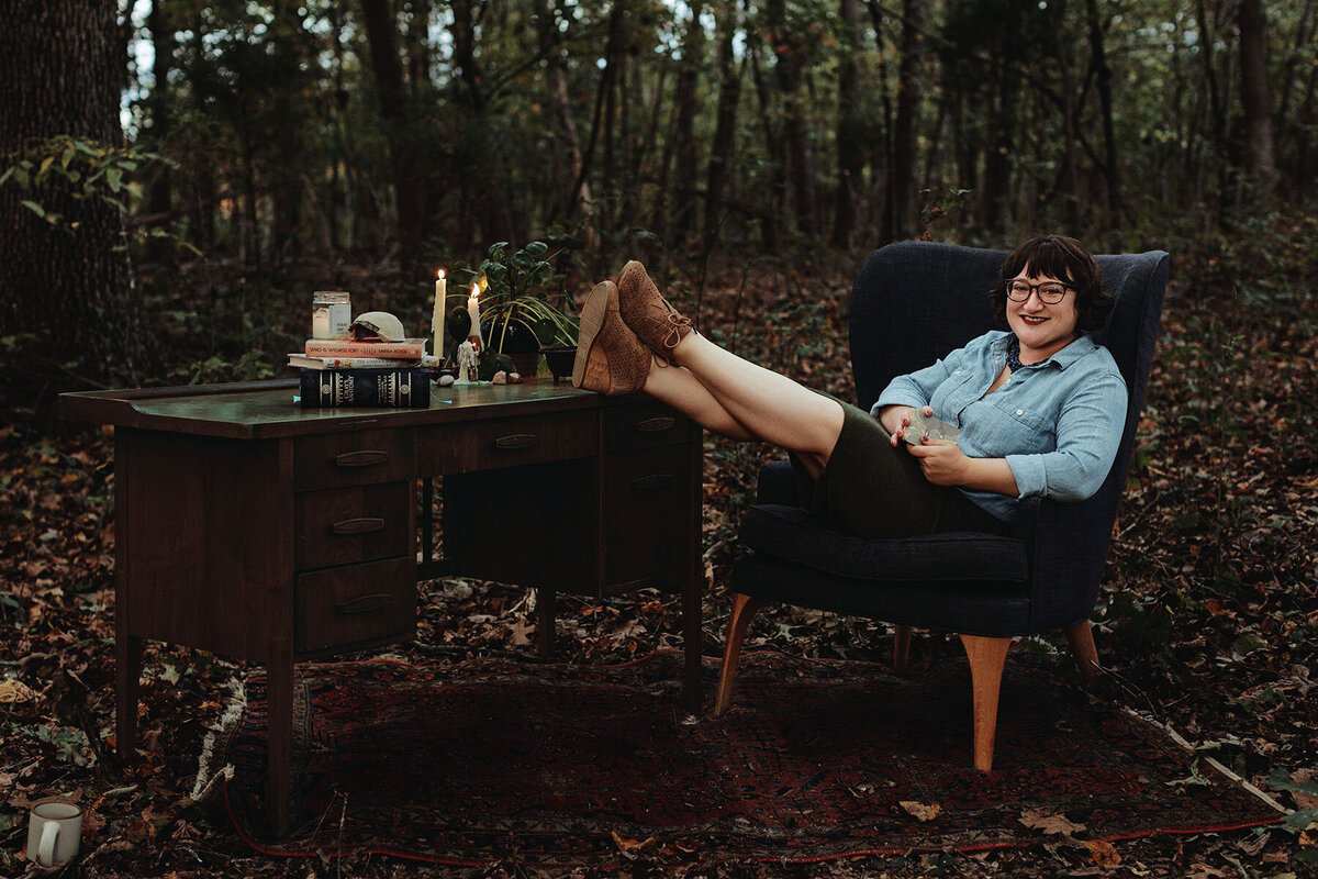 Ash sits at a table in the forest practicing energy work in front of a lit candle