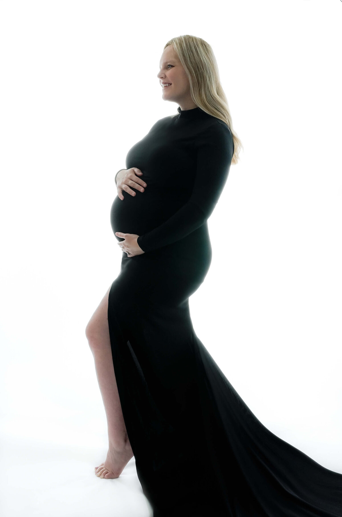 E. Benecki Photography photographs this expecting mother with back lighting. Mother is photographed wearing a long fitted black dress with a long train.