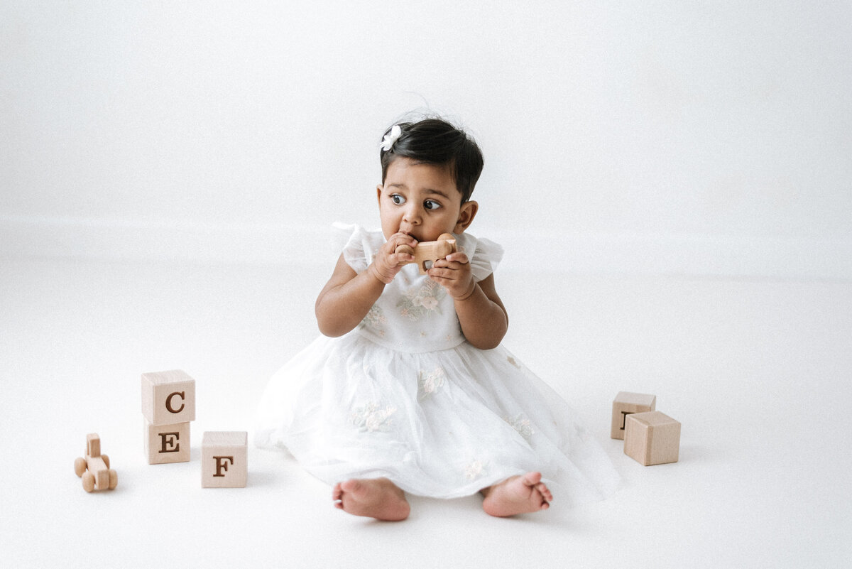 A baby girl playing with wooden toys at cake smash photoshoot in Billingshurst