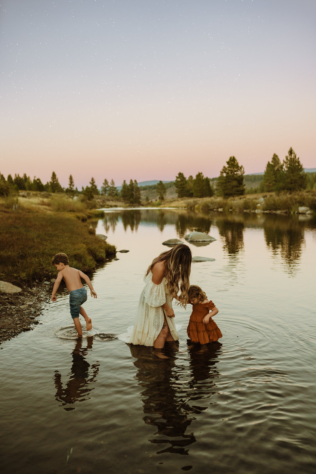Mom and her two kids are playing in the  Truckee river during dusk
