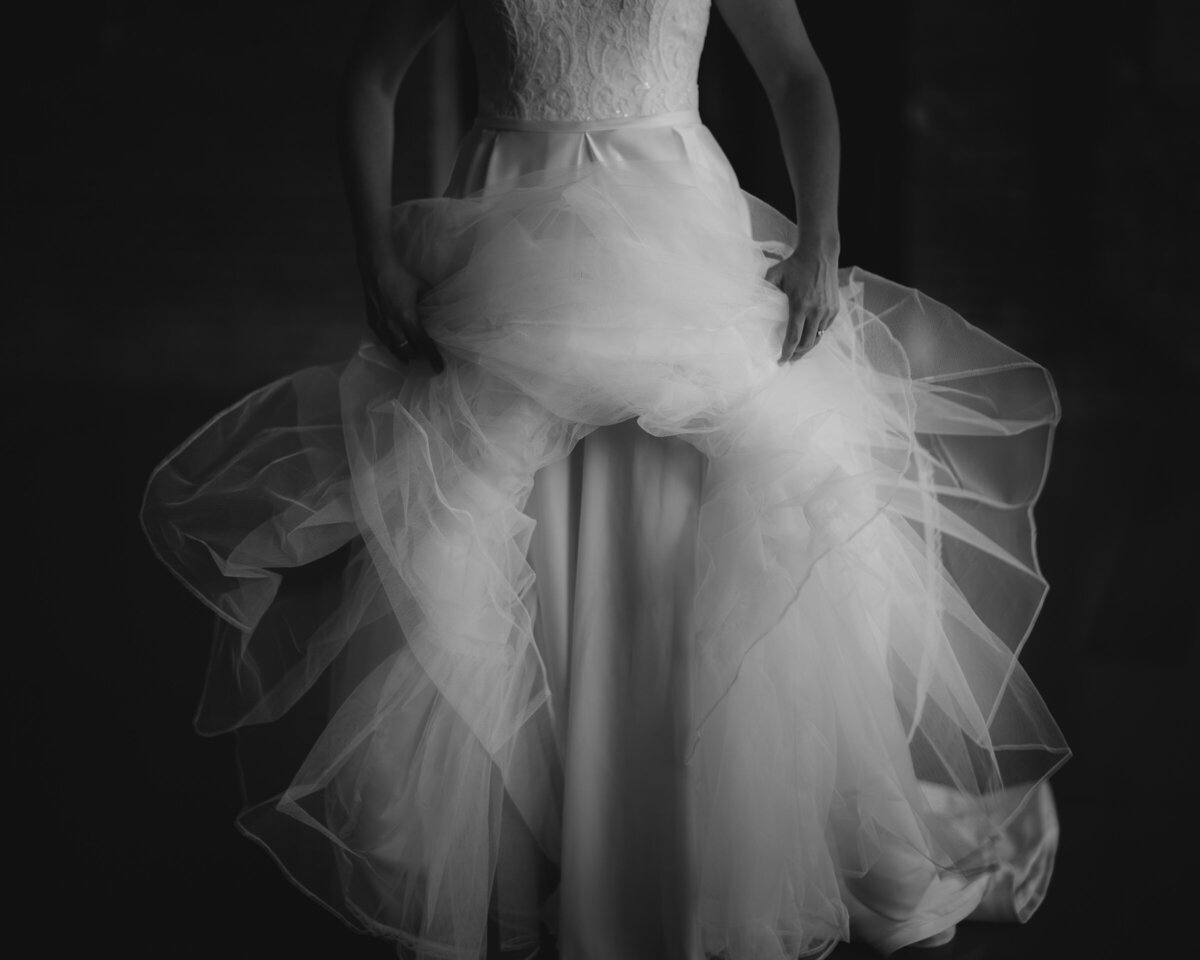 Artistic black and white close-up of a bride’s wedding gown and veil, focusing on the textures and layers of the fabric