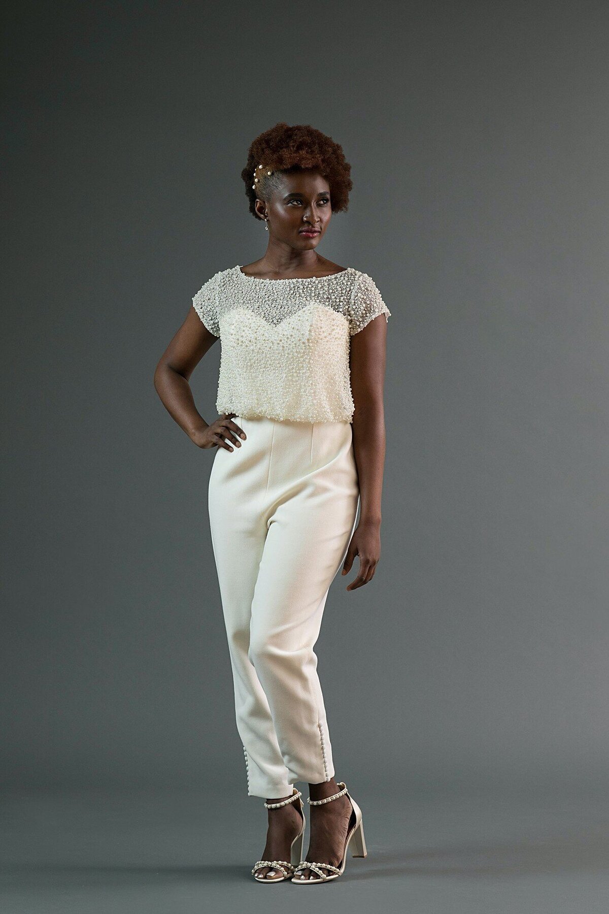 The Jonah bridal jumpsuit is made from a wool crepe cropped pant and strapless bodice foundation with a dense pearl net topper.