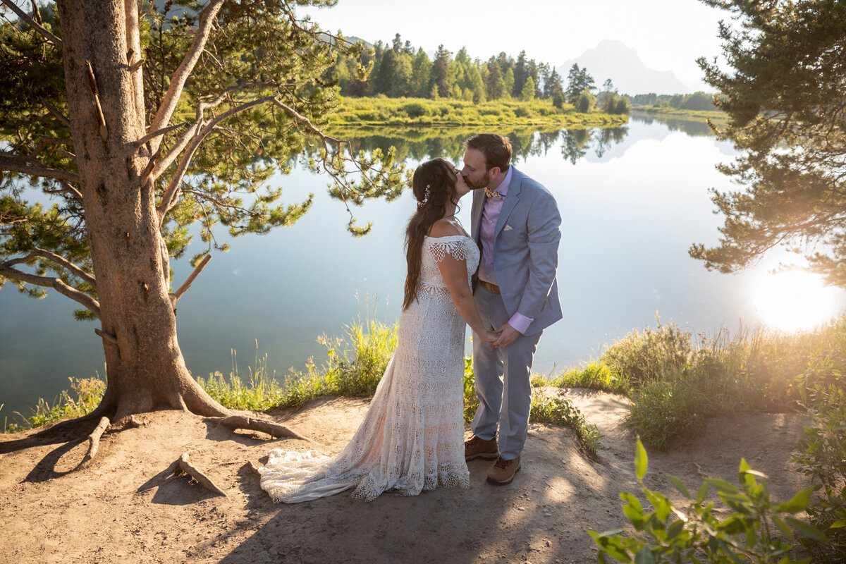 A bride and groom kiss next to a lake in Wyoming on their elopement day.