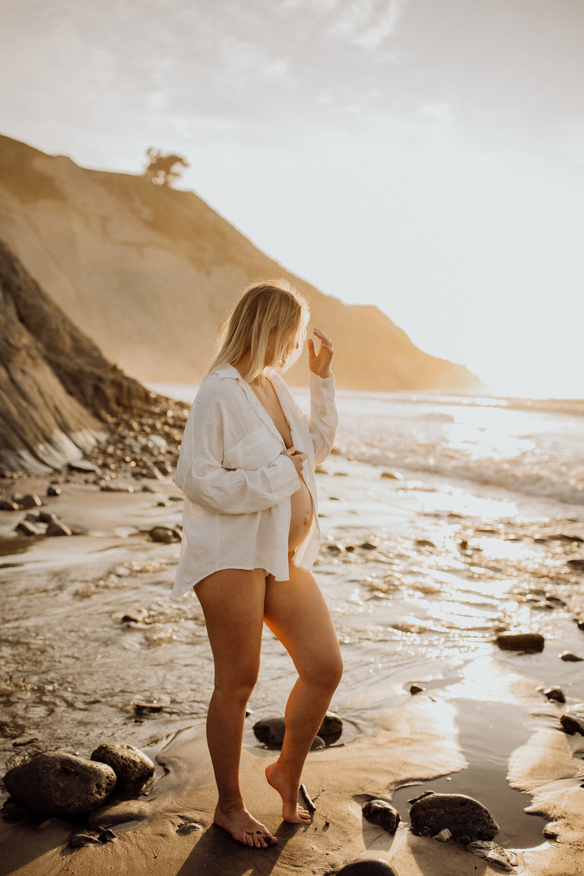 A mother to be wearing a shirt showing her bump during a sunset photoshoot at a popular christchurch beach with lucy jane photography