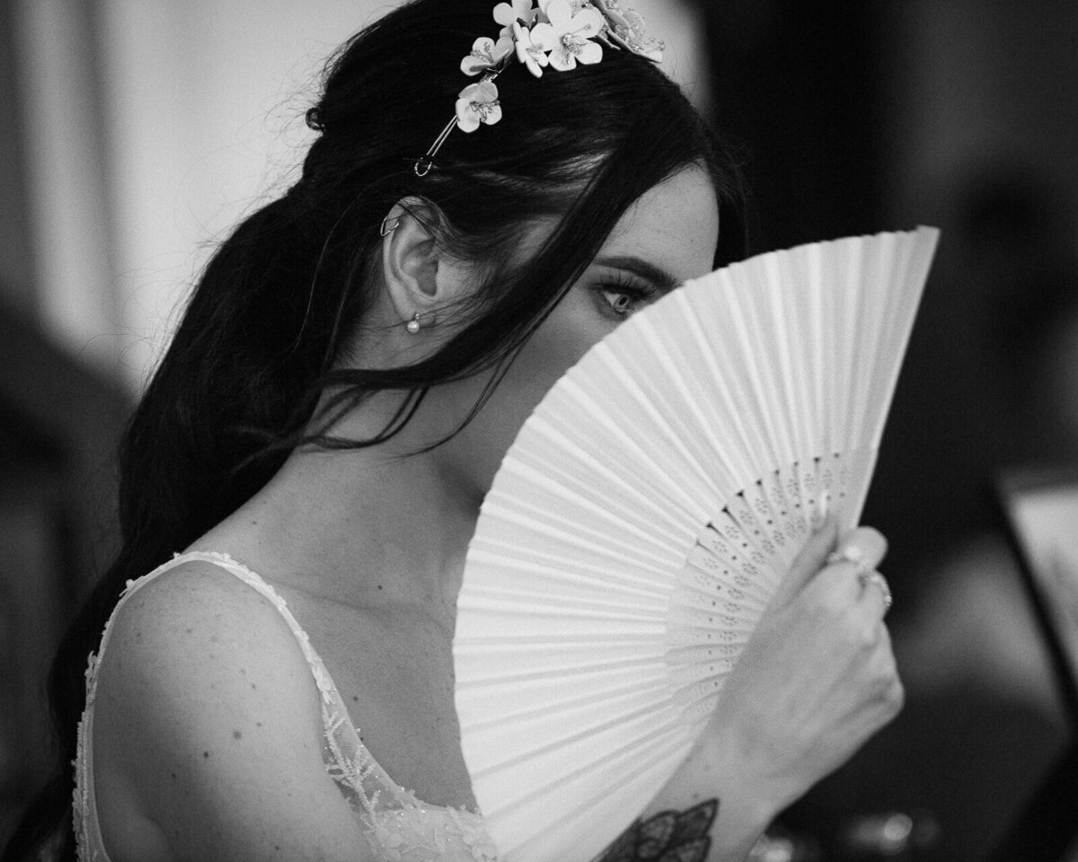 A bride hides behind a fan on her got wedding day.