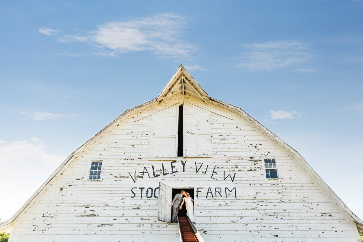 Couple kisses on top of a barn in front of a bright blue sky