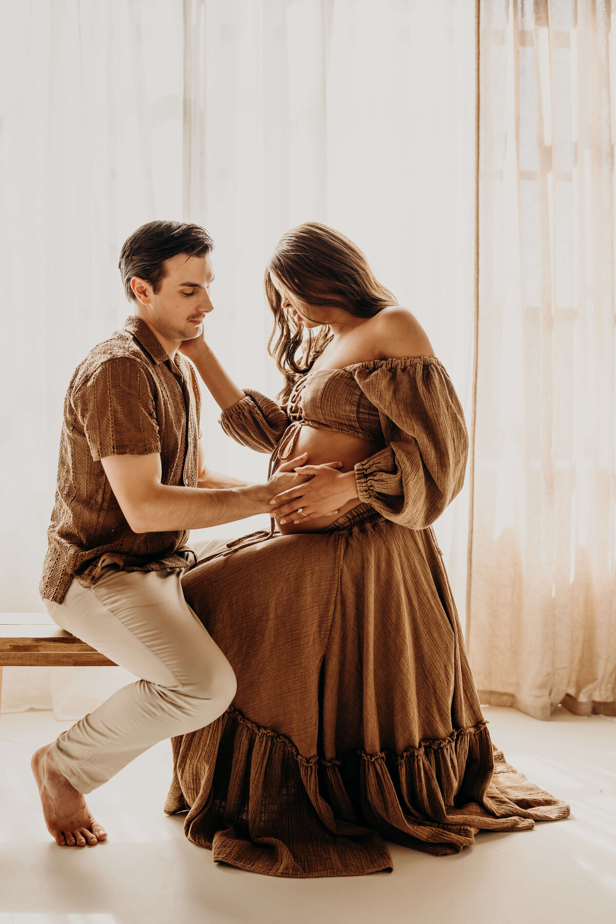 man and pregnant woman kneel on bench facing each other with legs intertwined