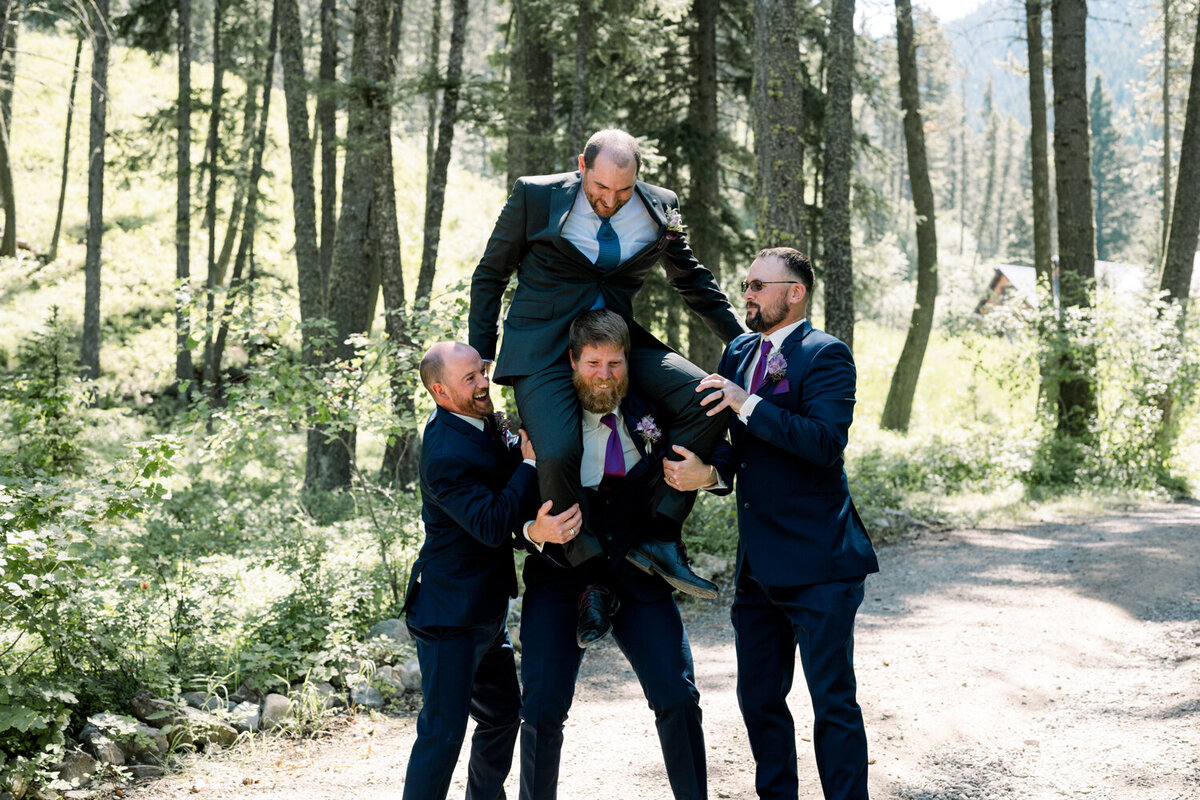 Groomsmen joyfully tossing the groom in the air during a summer wedding at The Woodlands at Cottonwood Canyon in Bozeman, MT.