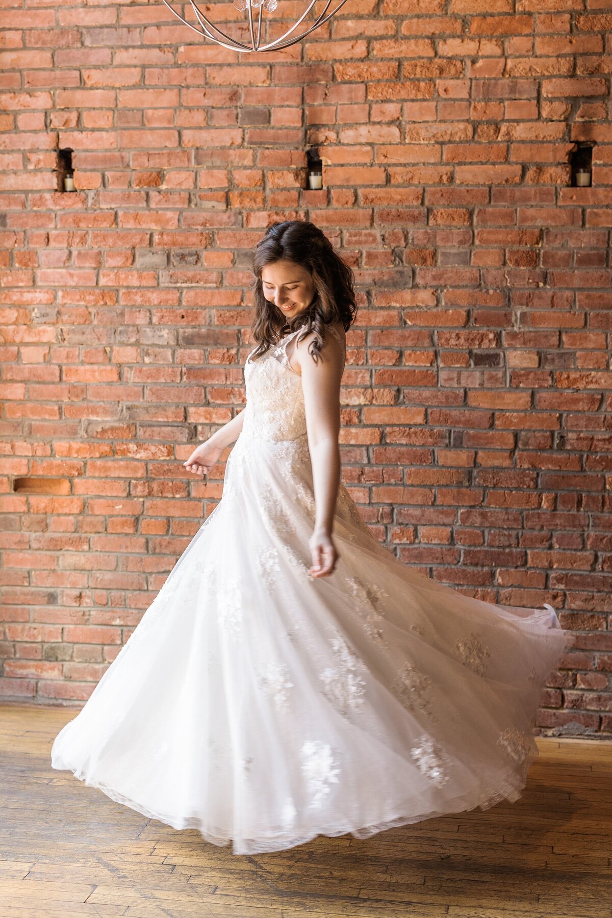 Portrait of a bride twirling her wedding dress on her wedding day in Plano, Texas. The bride is wearing a long flowing, detailed, white dress and twirls in front of an antique brick wall.
