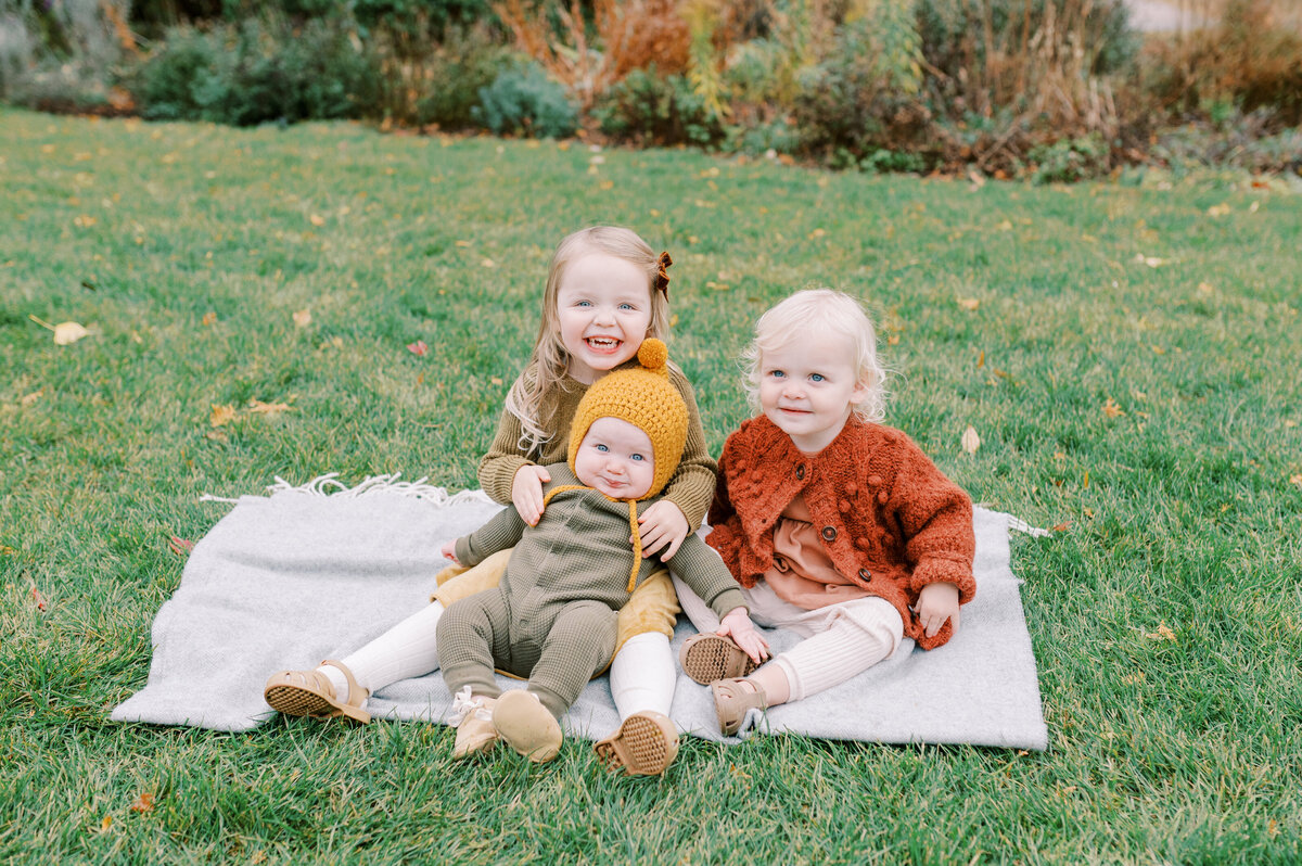 Three daughter's sitting on blanket in fall clothes