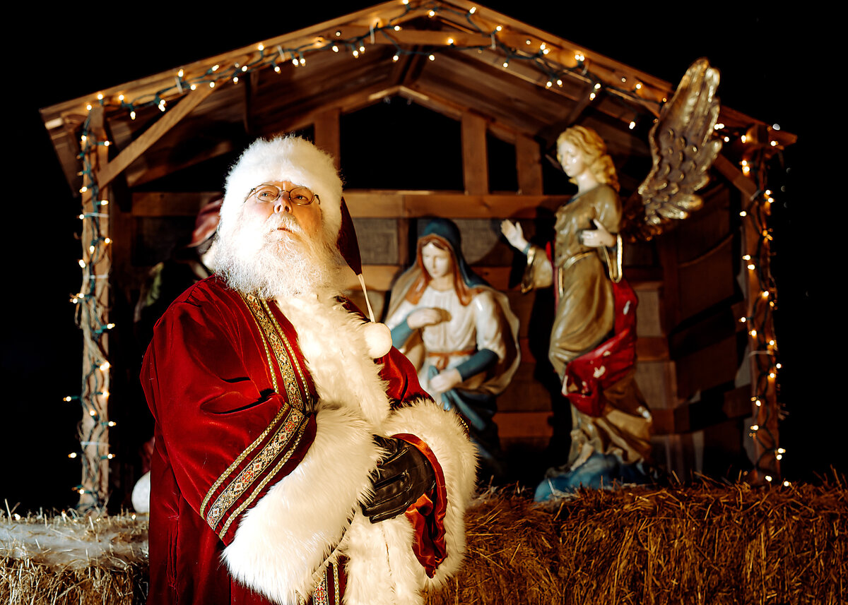 Branding portrait of Santa Claus wearing an old-fashioned robe in front of a manger at night for a South Shore MA Portrait Photographer.