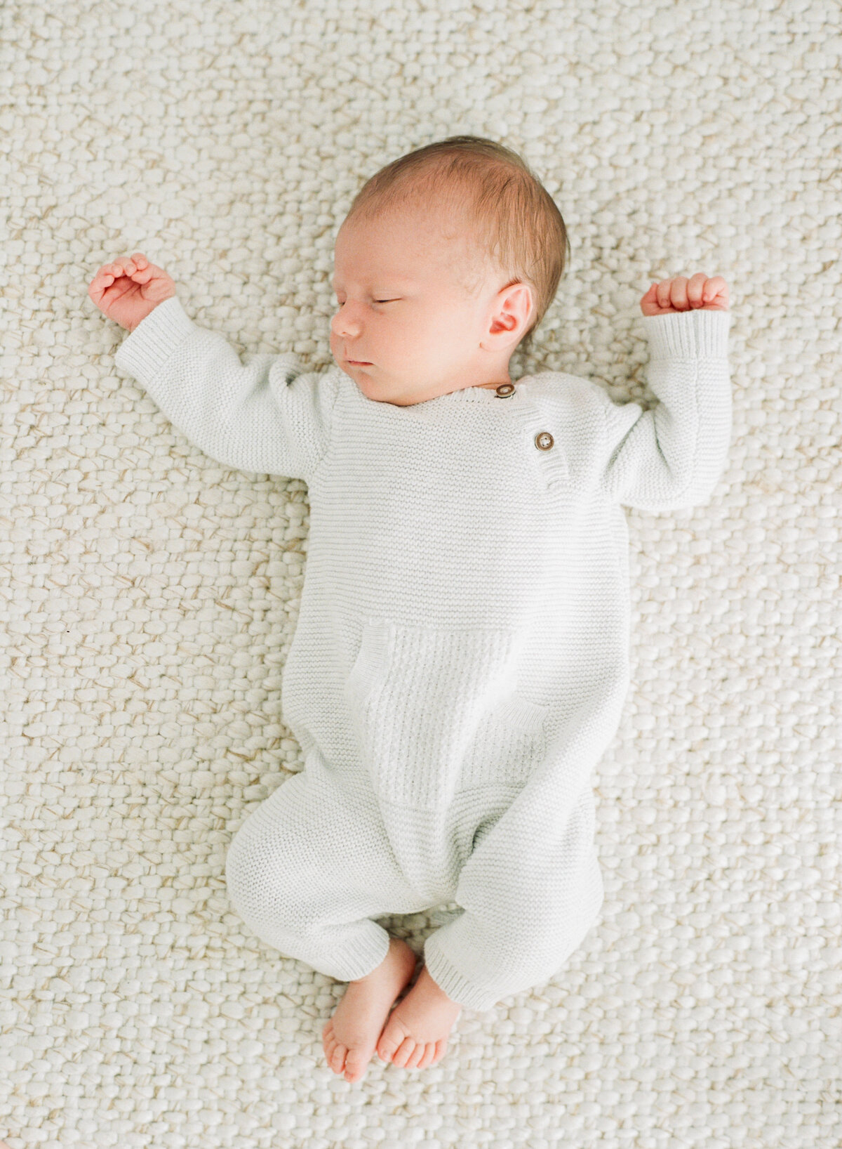 Baby lies on a textured blanket and sleeps while wearing a white newborn outfit during his Raleigh NC newborn session. Photo by Raleigh Newborn Photography A.J. Dunlap Photography.