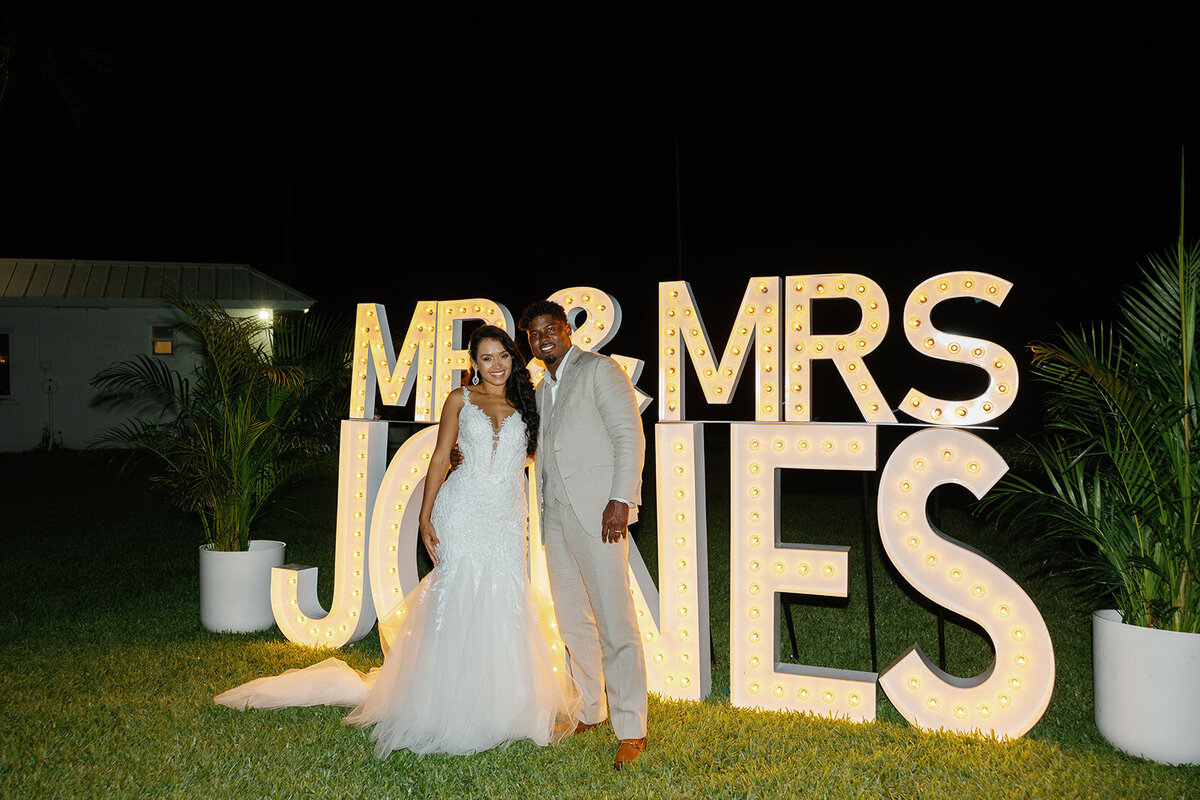 Newlyweds Andressa and Jonathan pose in front of their glowing "Mr. & Mrs. Jones" sign during their elegant Islamorada wedding reception. Captured by Claudia Amalia, Islamorada wedding photographer.