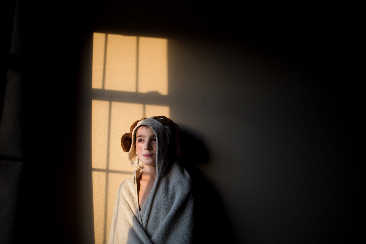 child in hooded towel standing in the window light