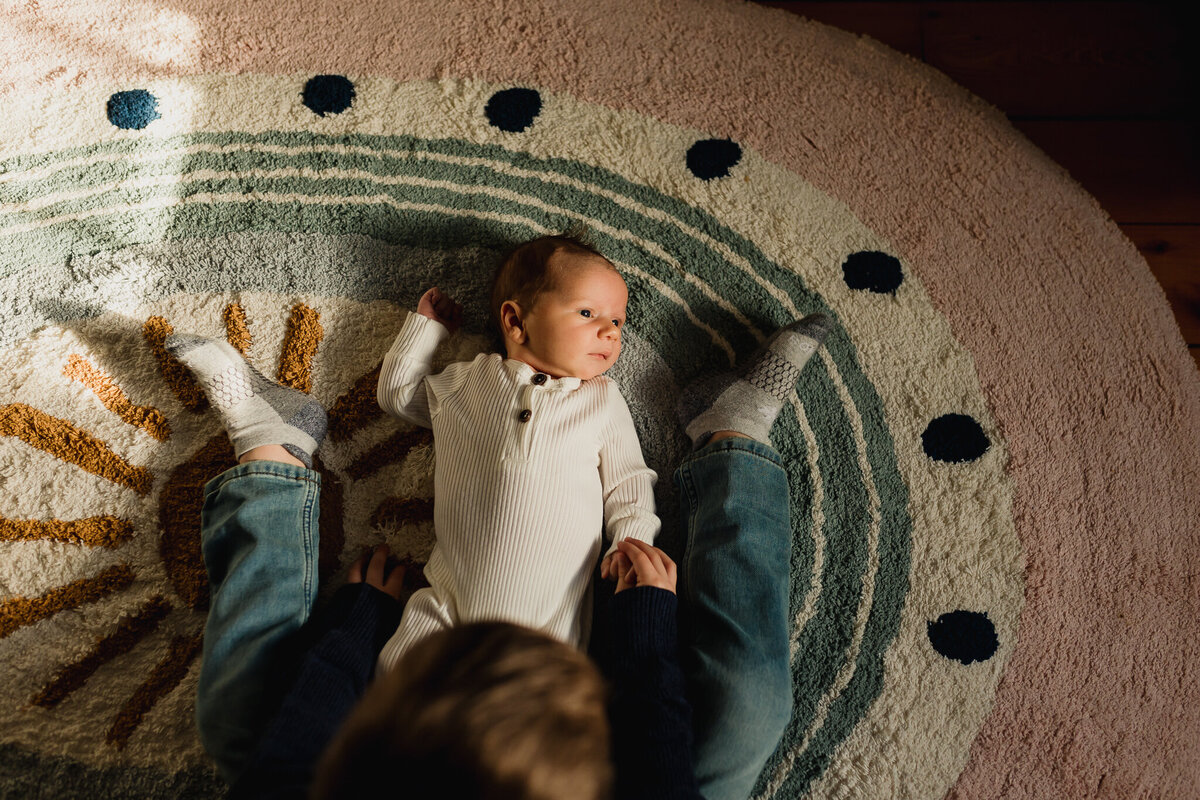 Infant photographer capturing a big brother and newborn rest on nursery rug
