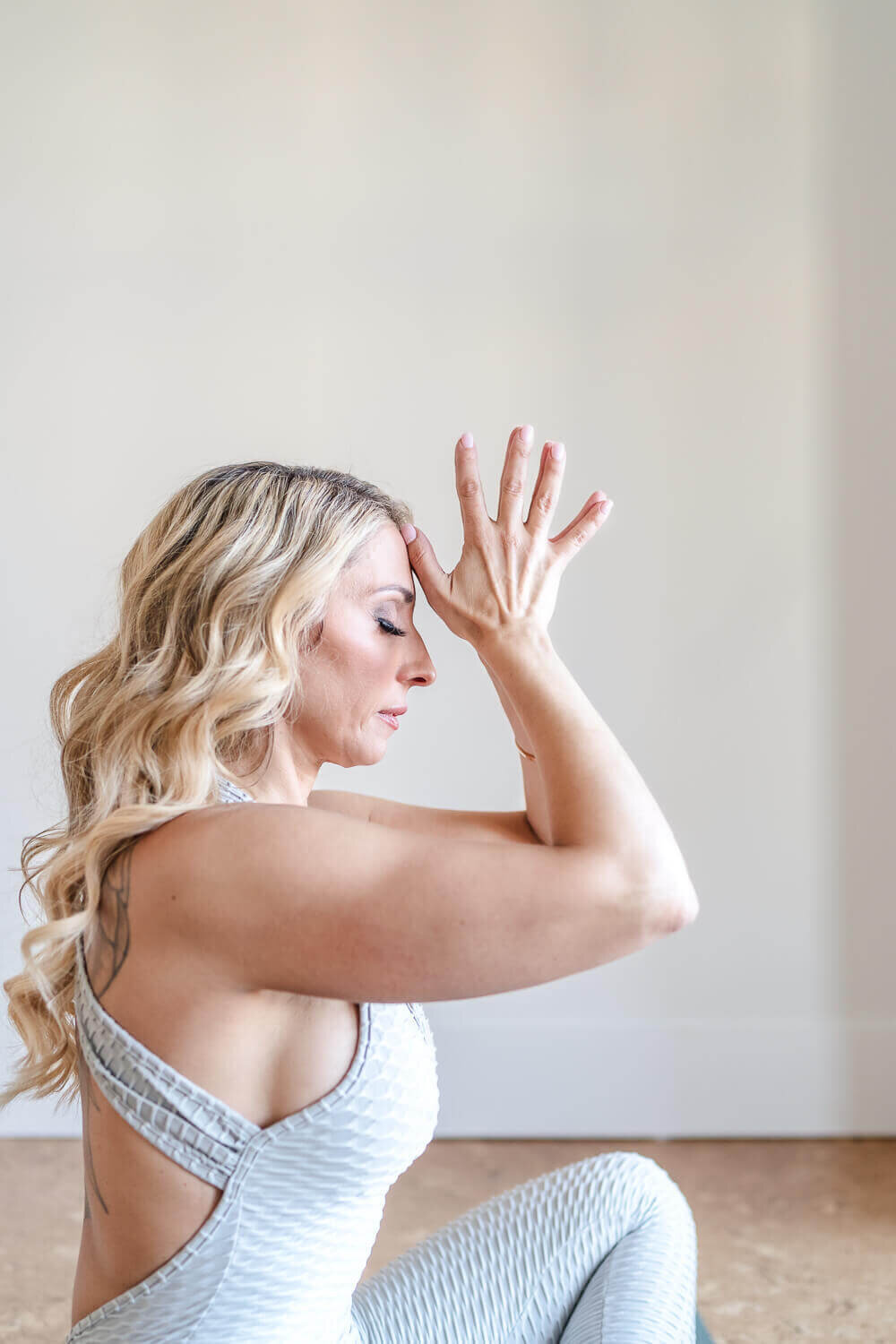 Female entrepreneur wearing grey active wear holding her hands to her forehead during meditation.