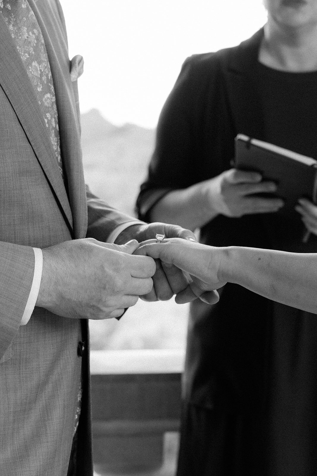 Black and white photo of couple holding hands while exchanging rings during their elopement ceremony. 