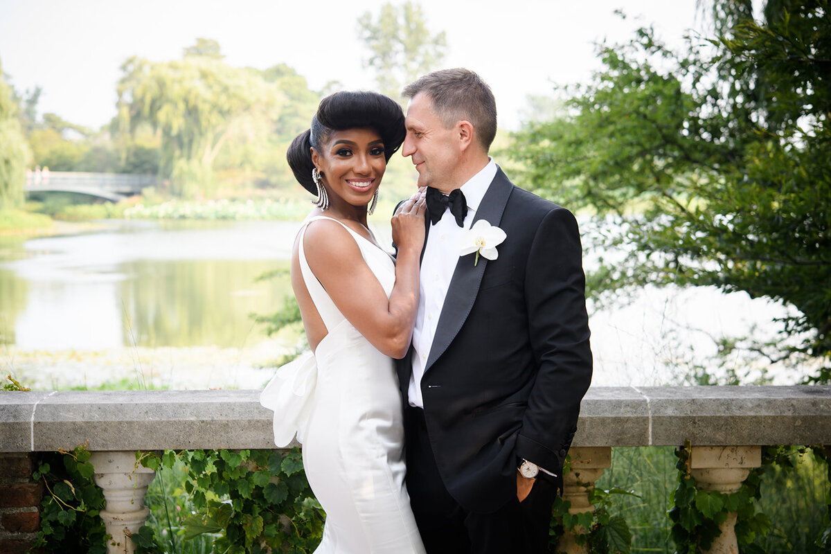Bride and groom pose by a serene lake, enveloped in natural beauty.