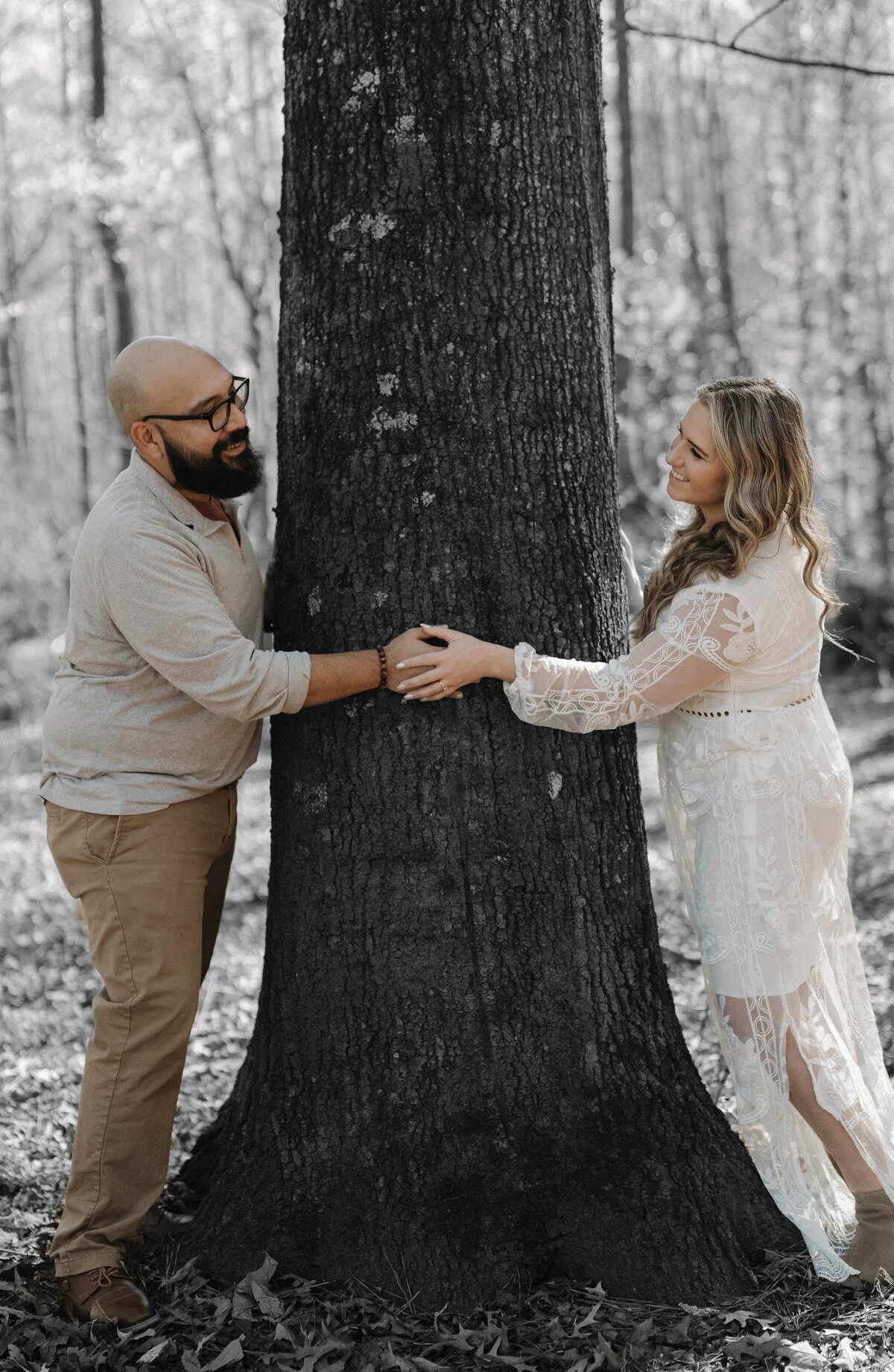A couple embracing a tree in a wooded area during a photoshoot