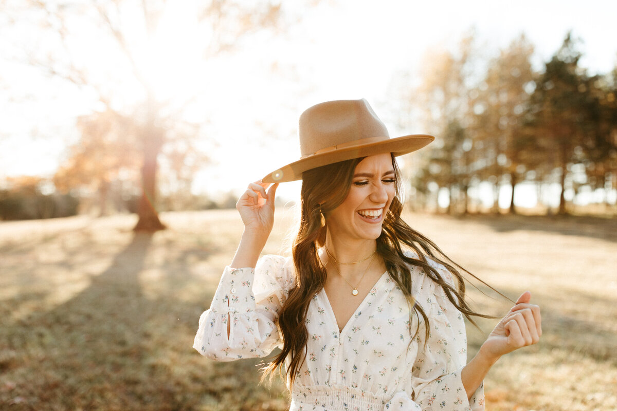 High school senior smiling while holding hat and twirling her hair
