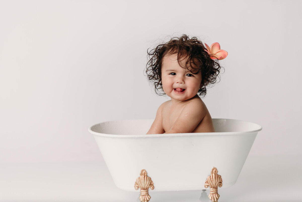 Smiling one year old girl sitting in miniature white bathtub