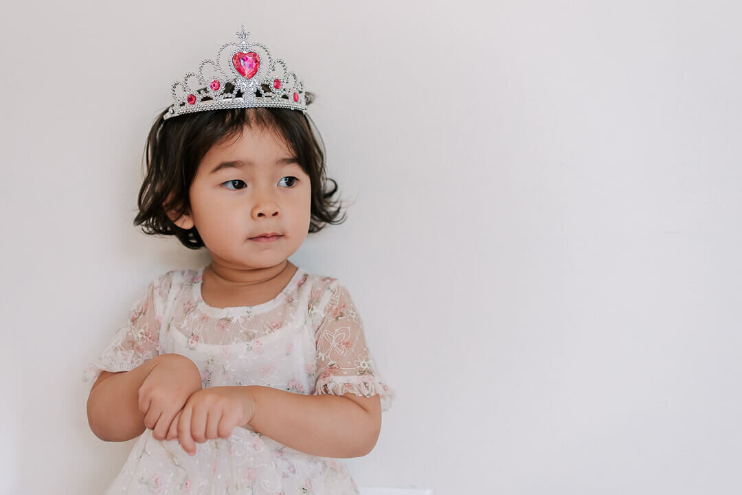 A little girl wearing a floral dress and a crown on her head