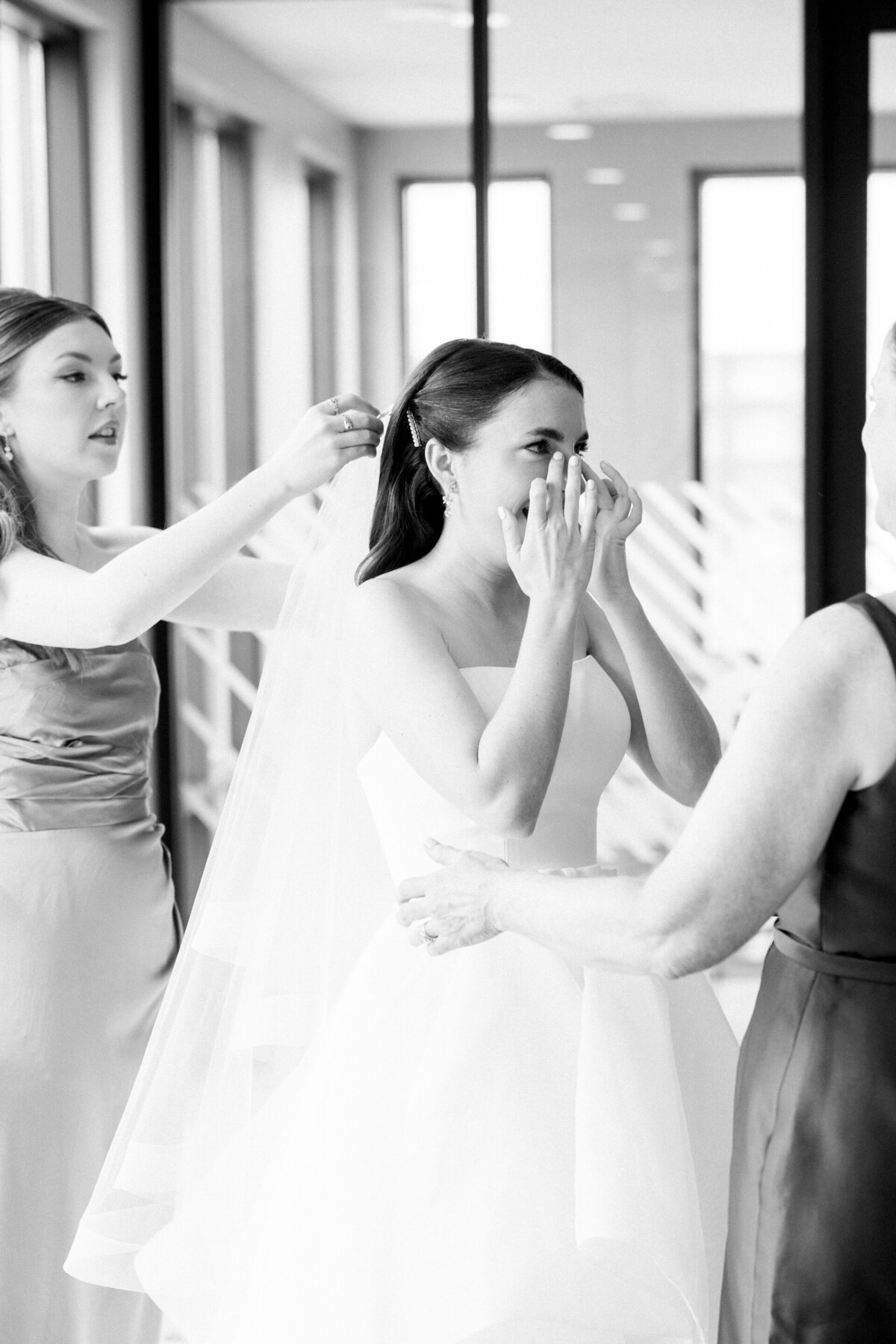 bride crying as other women help her get dressed for her wedding