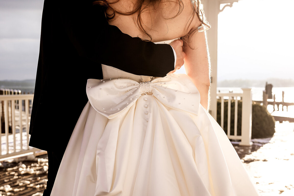 Groom with his arm around brides back with bride with beautiful bow on the back of her gown