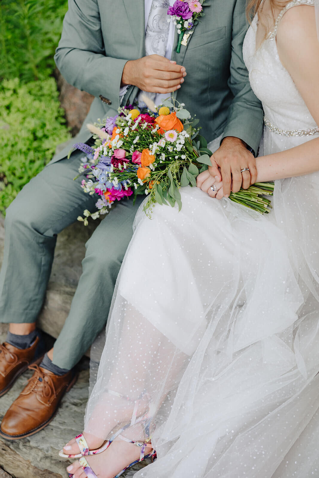 Close up of bride and groom sat down with floral bouquet holding hands