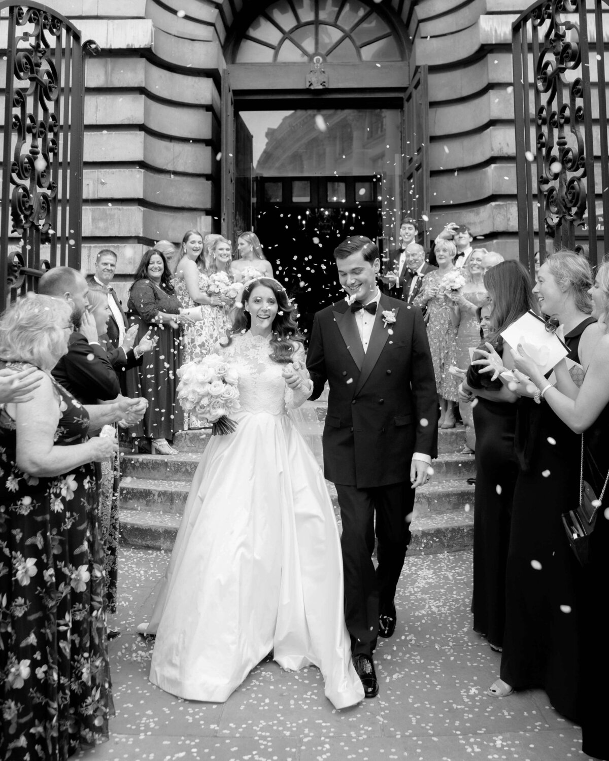 bride and groom exit their london church wedding ceremony walking down the steps outside towards the gates as guests throw confetti over them