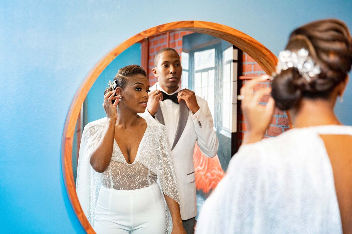 A bride adjusting her earrings while her groom adjusts his bow tie.