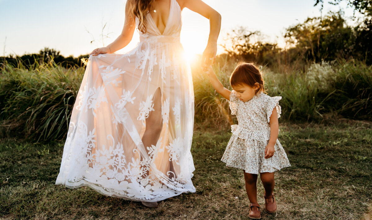 Family Photographer, mom and baby girl walk in the grass together near the forest