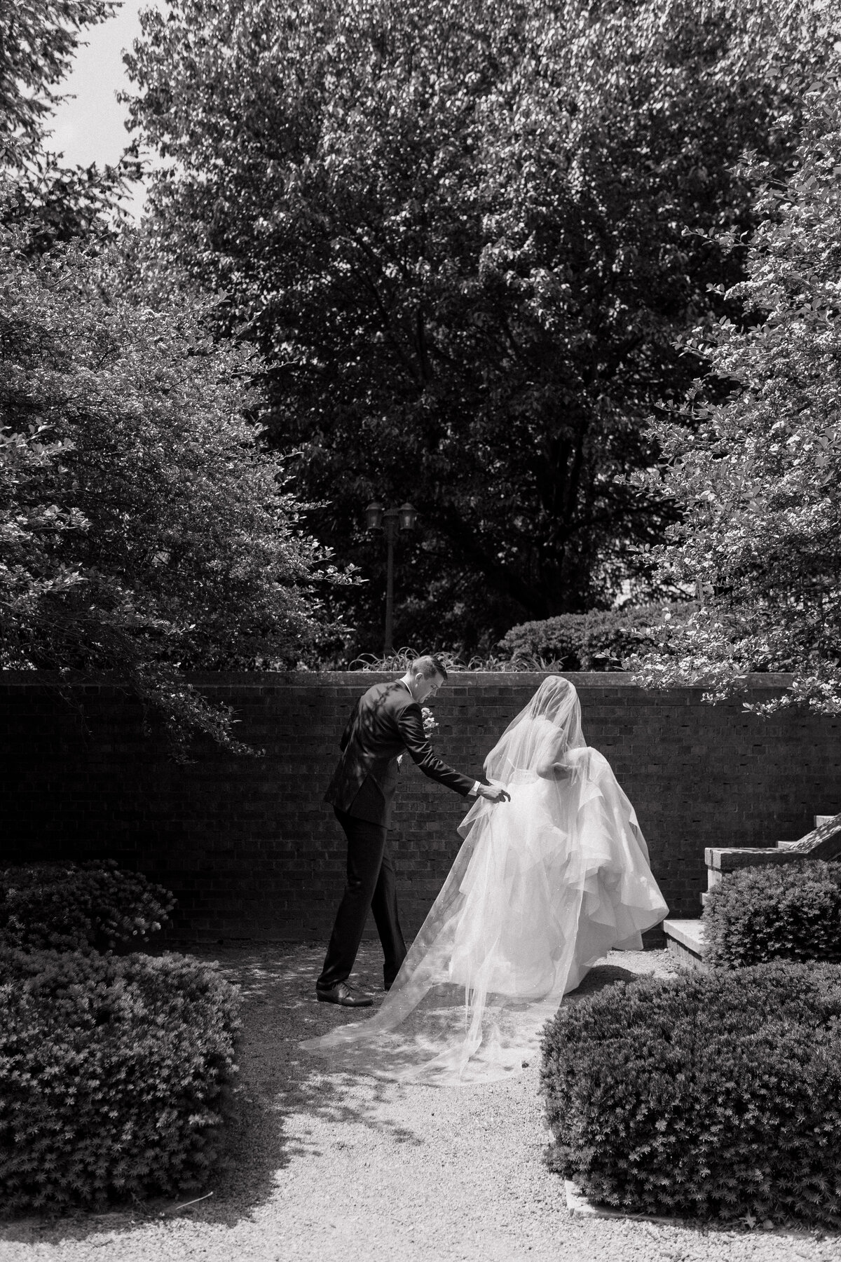 Groom helps bride carry her dress and veil as she walks up the stairs at a historic Mansion. Photo by Anna Brace, who specializes in Kansas City Wedding Photography.