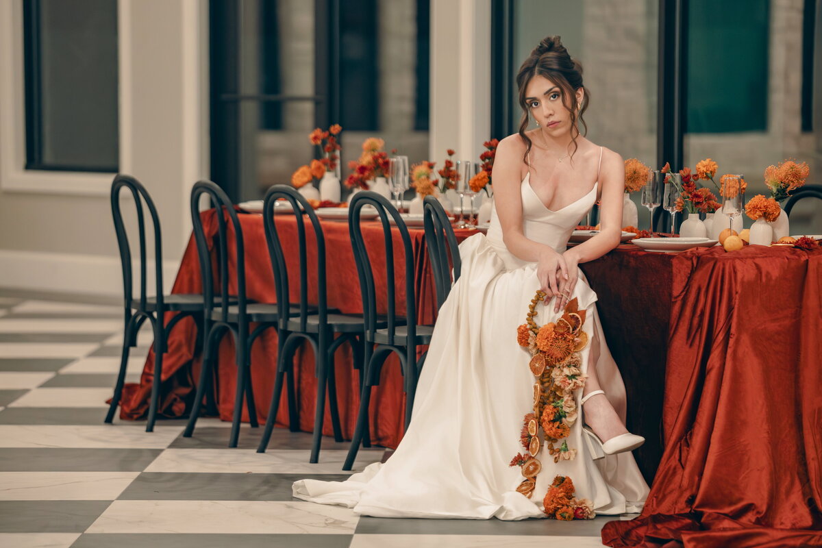 Salt Lake City bridal photographer capturing an editorial bride seated beside a rust-colored wedding tablescape with fall florals. Moonlit Photo Utah wedding photography featuring modern, cinematic bridal portraits and luxury event styling.