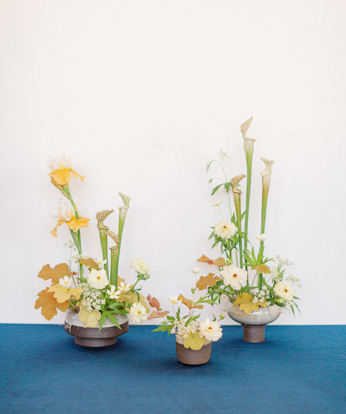 Three small floral arrangements of orange leaves, white flowers, and tall lilies.