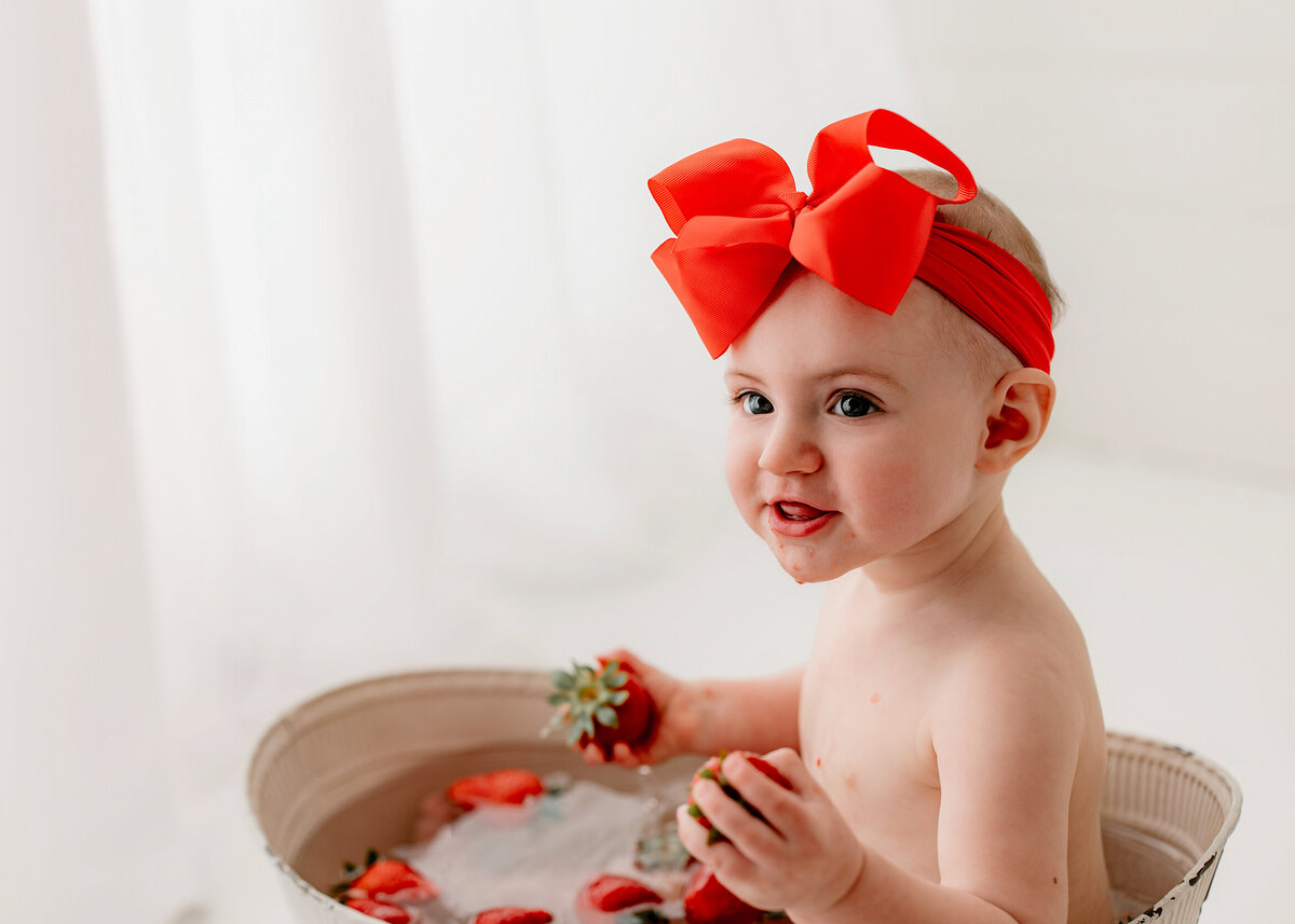one year old baby girl in a strawberry bath after milestone first birthday photo session in clarksville tn