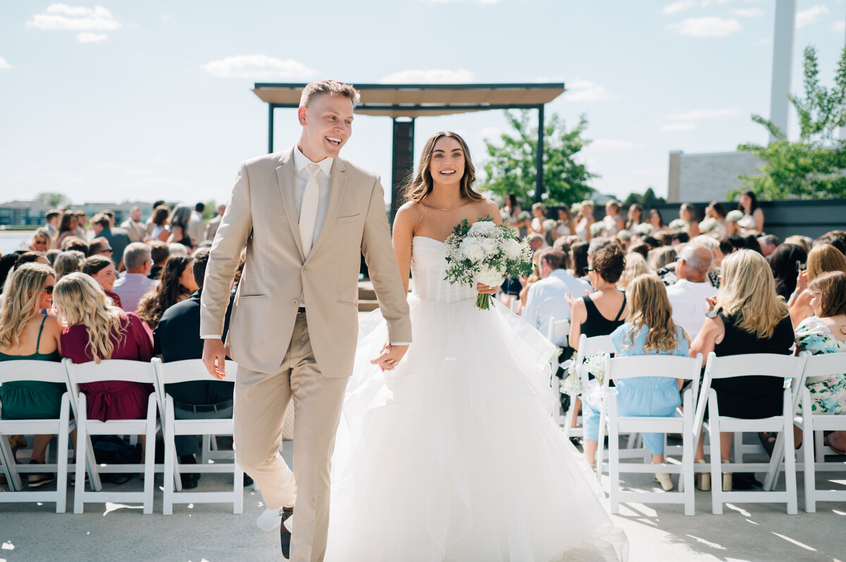 Bride and groom exit their ceremony hand in hand as their guests cheer at A View at West Shores. Photo by Anna Brace, who specializes in NE Wedding Photography.