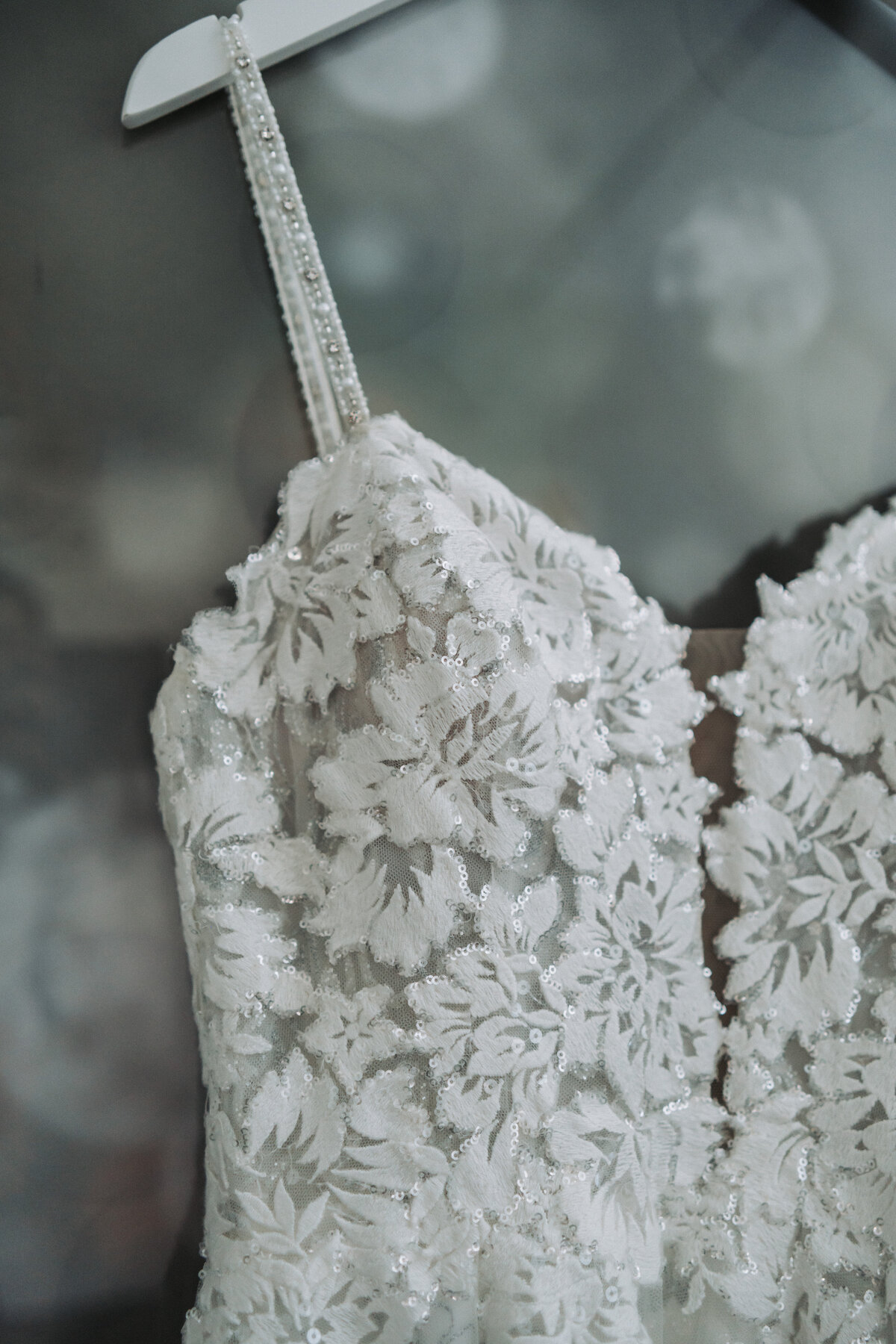 A close-up of an exquisite wedding dress hanging, showcasing intricate lace and beaded strap details, beautifully captured at the Hampton Roads Event Center by Quinn Photography LLC.