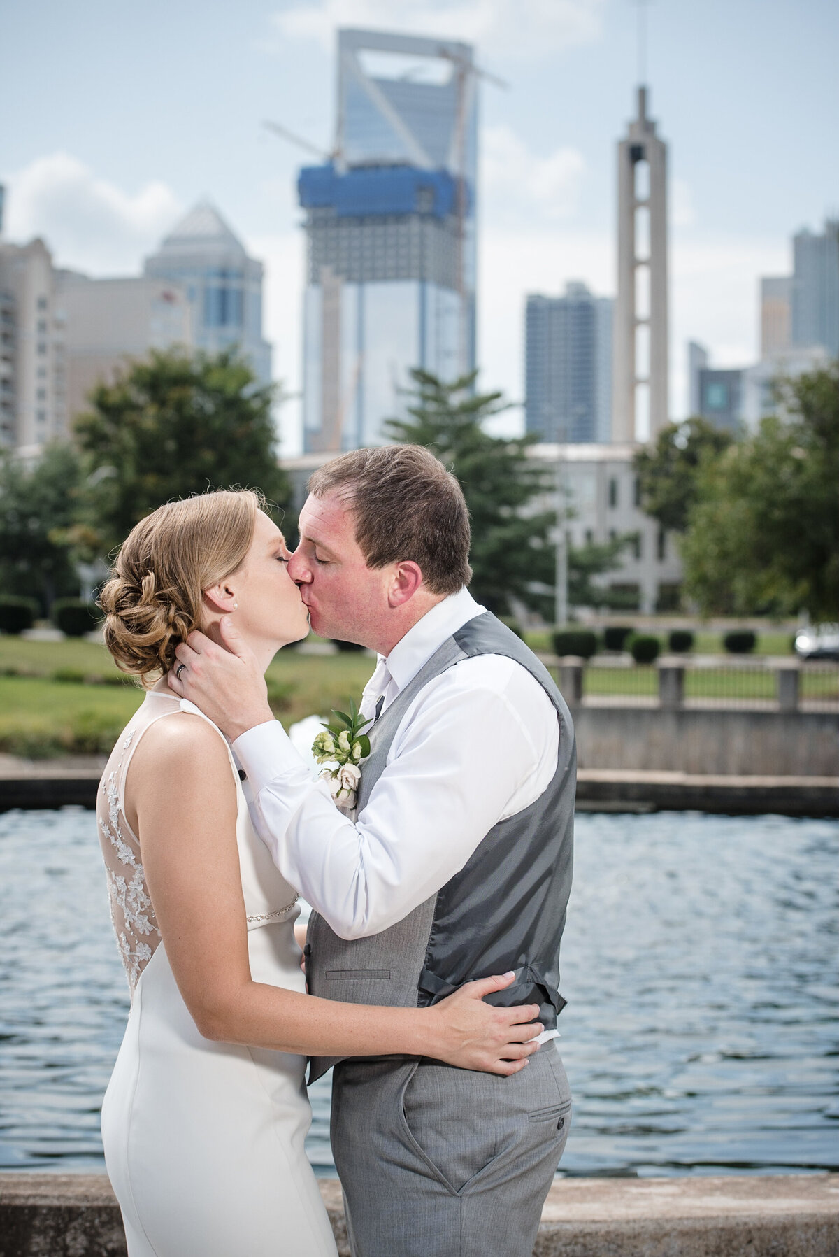 Bride and groom sharing a kiss in Marshall Park with the Charlotte city skyline in the background on their wedding day at the Omni in uptown by Charlotte wedding photographer DeLong Photography