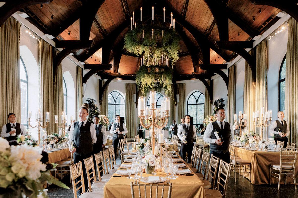 The waiters line up inside the elegant wedding reception room with candle chandeliers, bronze tables and chairs.