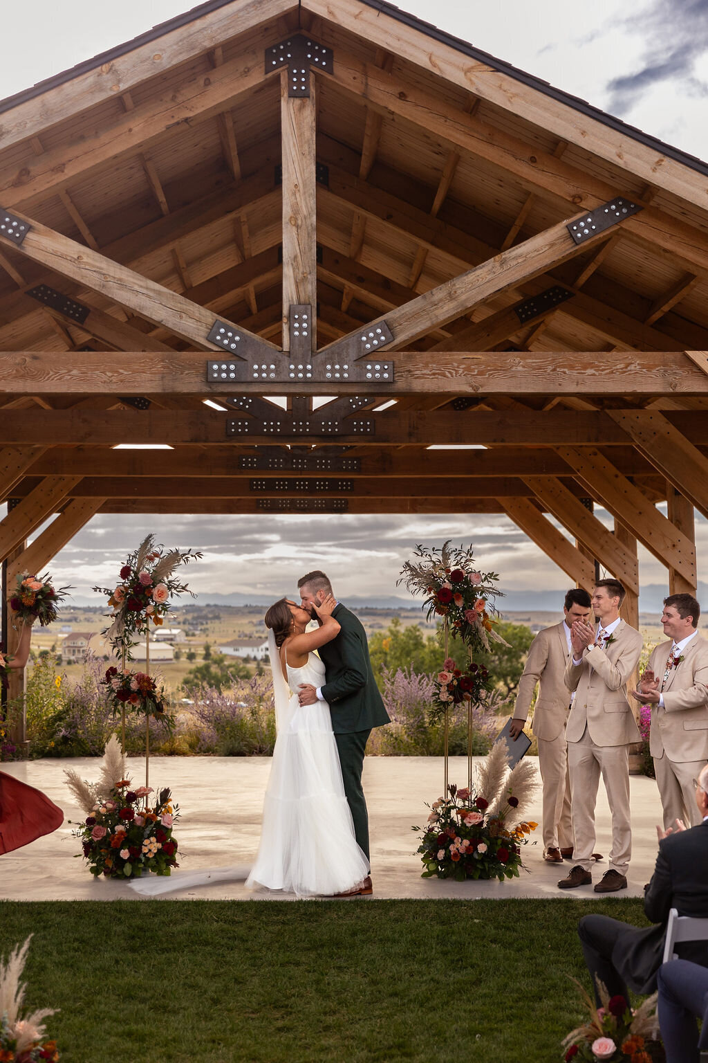 Bride and groom share their first kiss with burgundy fall colored flower arrangements during their wedding ceremony at Bonnie Blues Event Venue.