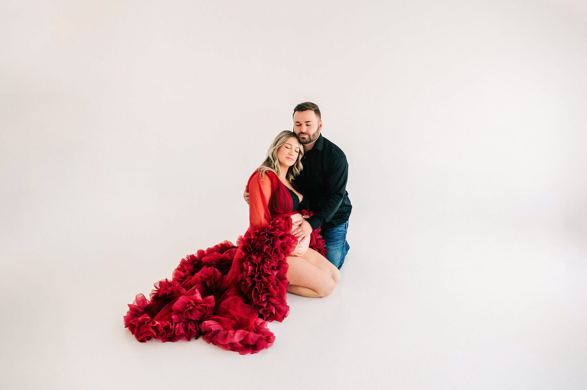 pregnant couple kneeling on floor cuddling in maternity photography studio in Springfield MO