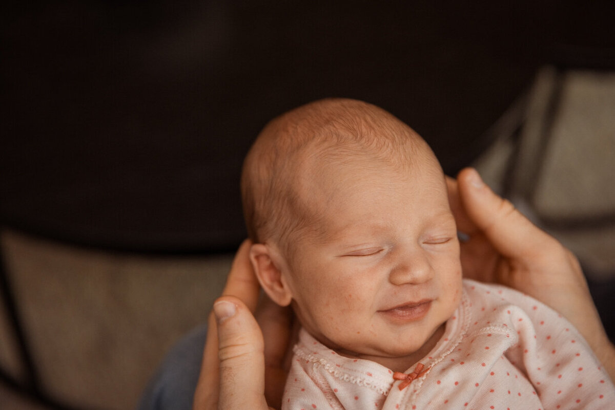 Livsstilsfoto portrett av en baby som smiler med lukkede øyne. Ligger i fars hender.